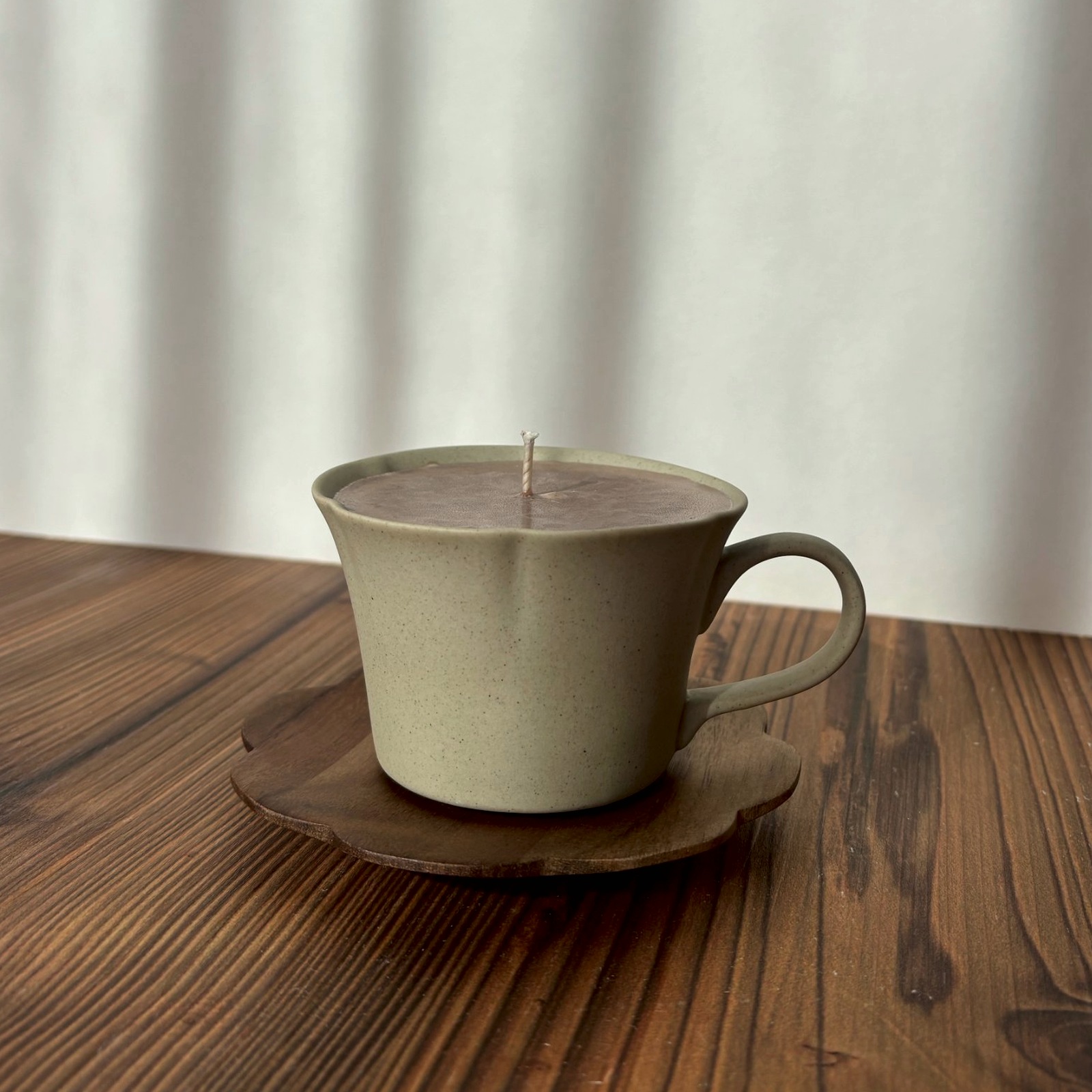 DUFTKERZE IN EINER GESPRENKELTEN TASSE MIT HENKEL AUF BLÜTENFÖRMIGER HOLZUNTERTASSE